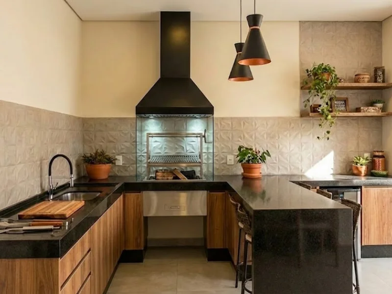 Coifa de parede preta instalada em área gourmet com churrasqueira e bancada preta