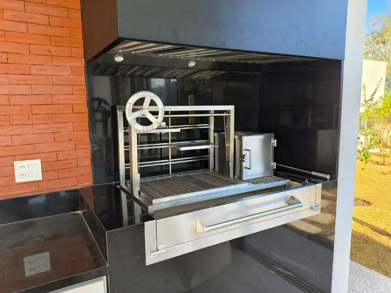Coifa de embutir preta instalada sobre churrasqueira com sistema de parrilla e motor